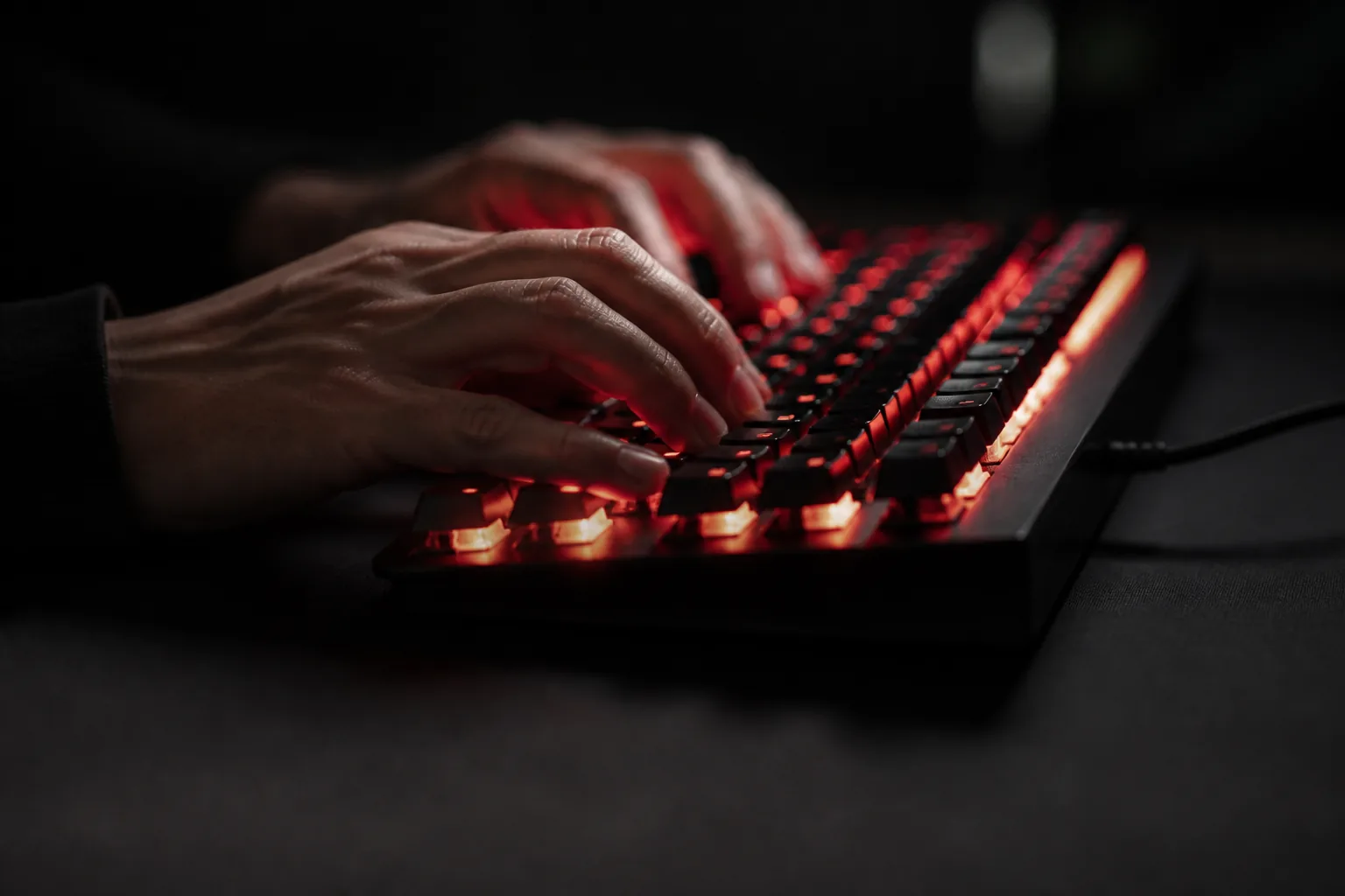 Manos escribiendo sobre un teclado mecánico retroiluminado en rojo